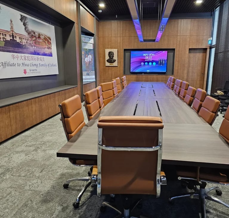 Modern conference room with long white table, tan leather chairs, projection screen on left, large display monitor at end, wood paneling, and blue accent lighting